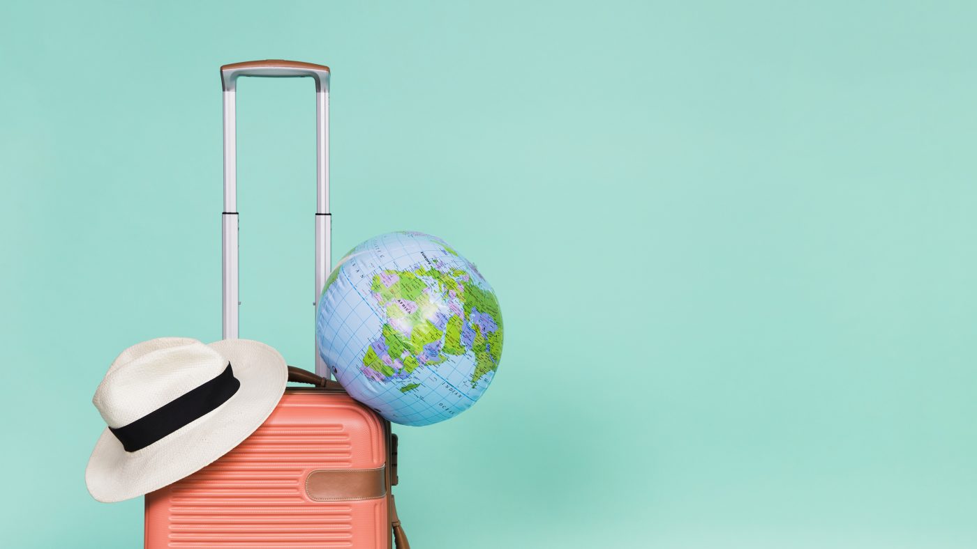 light blue background with pink suitcase, world globe and hat